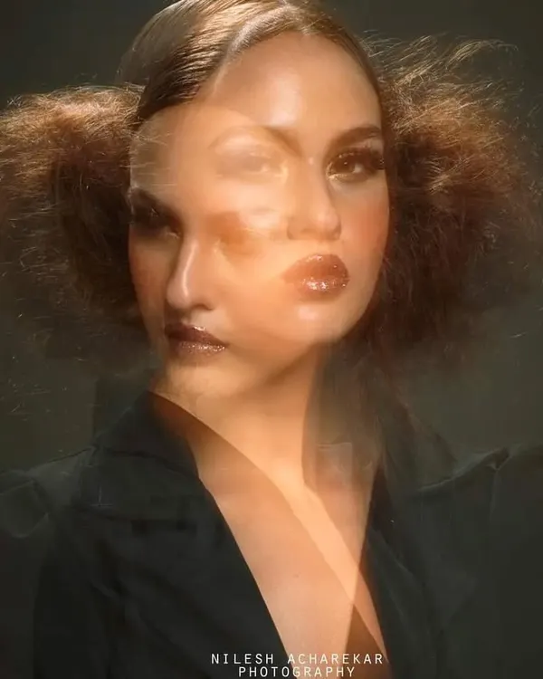 An artistic editorial shot using a double exposure technique. The makeup is glamorous and defined, contributing to the abstract and dreamlike quality of the final photograph.