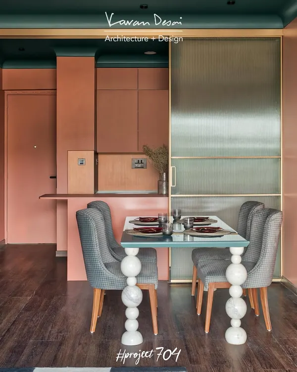 The dining area in Project 704 is a showcase of custom design and bold color. The table features a simple glass top on legs made of individually stacked marble spheres, set against a warm terracotta wall.