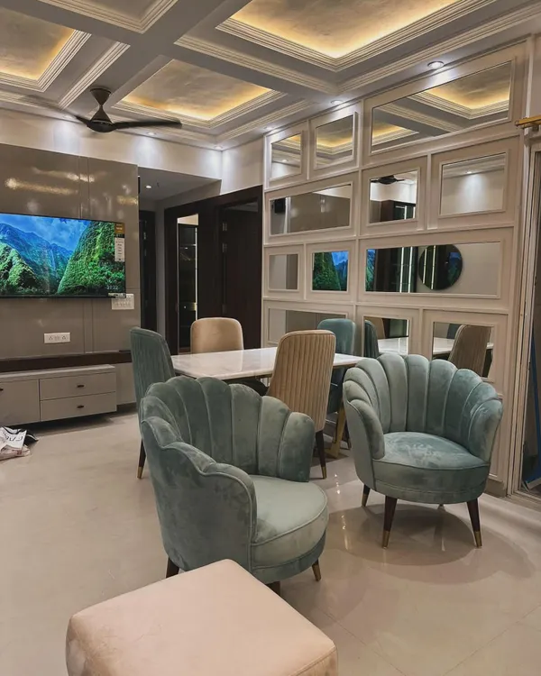 This open-plan living and dining area combines elegance with a welcoming ambiance. We used plush, shell-back accent chairs in a soft teal velvet to add a pop of color, complemented by a mirrored grid wall that enhances the sense of space and light. The design focuses on creating distinct zones for lounging and dining while maintaining a cohesive, luxurious feel.