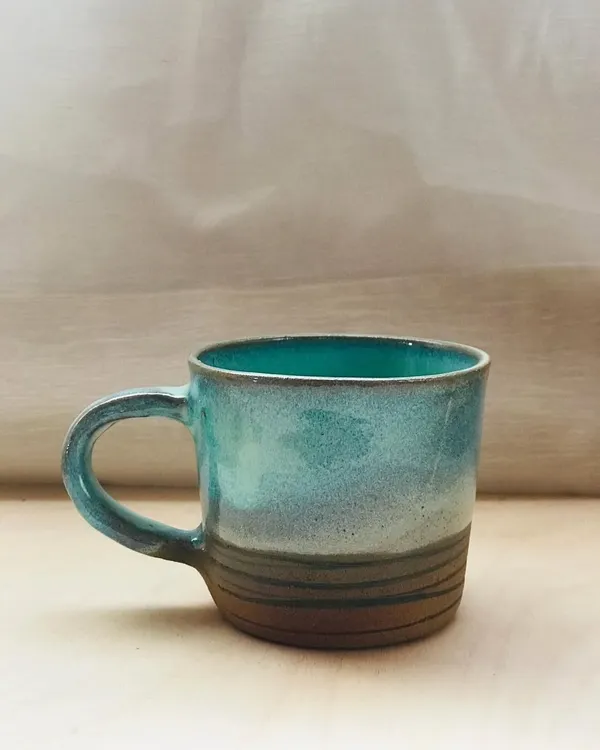 The Flow Mug, designed for slow sipping. This piece features a beautiful ocean-blue glaze over a textured, earth-toned base, complete with a comfortable handle for your morning brew.