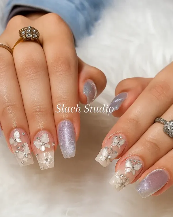 This elegant set on coffin extensions features a combination of shimmery lilac polish and nails with 3D sculpted white flowers and rhinestone details. It's a perfect example of detailed bridal or special occasion nail art.