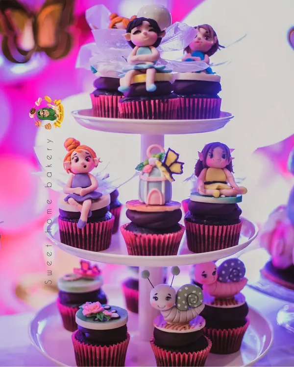 A beautiful display of enchanted forest themed cupcakes. Each cupcake is a work of art, topped with a unique, hand-sculpted figurine like a fairy, a snail, or a butterfly house.