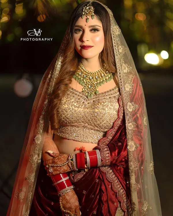 A stunning full-length portrait of a bride in her magnificent red and gold wedding lehenga. Her confident pose and direct gaze capture the essence of a modern, royal bride.