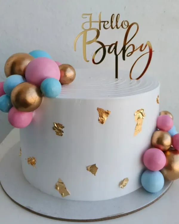 An elegant baby shower cake with pink, blue, and gold decorative balls and gold leaf accents. A beautiful way to say "Hello Baby."