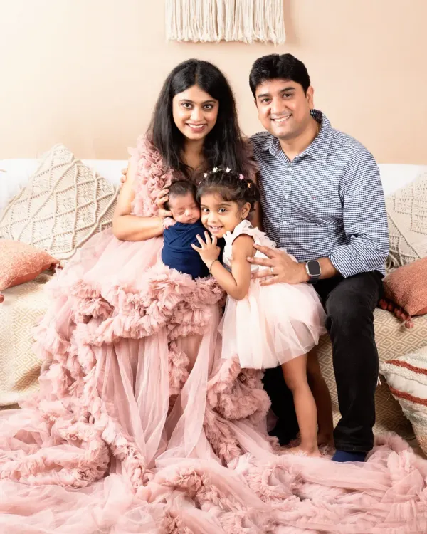 A beautiful family of four portrait, with mom in a stunning pink gown holding her newborn son while dad and big sister gather close.