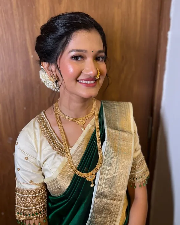 A classic engagement look. The bride is glowing in a dark green saree with a contrasting cream blouse. Her makeup is soft and dewy, and her hair is in a beautiful bun adorned with gajra.