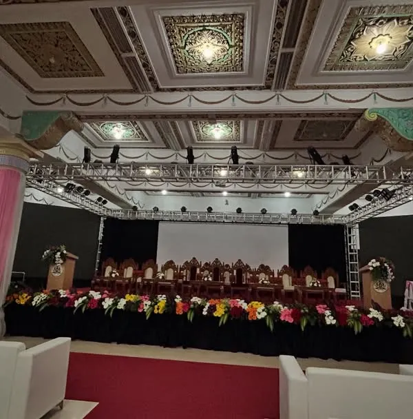 A wide-angle view of a formal event hall we prepared for a government meeting. The setup includes a complete stage with a lighting truss, a red carpet aisle, and organized seating for the audience.