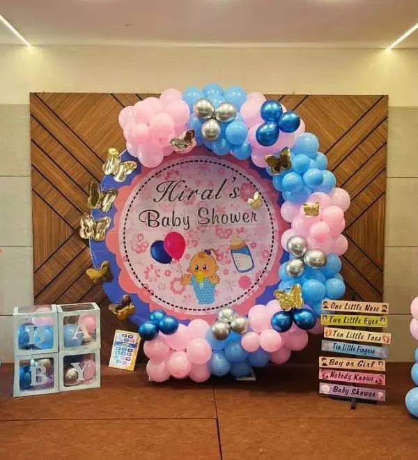 A classic baby shower setup with a 'Boy or Girl?' theme. The circular backdrop for 'Hiral's Baby Shower' is framed by pink and blue balloons, with cute baby cutouts on either side.