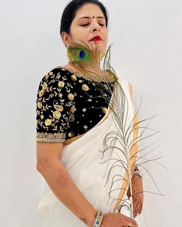 Celebrating Janmashtami with a beautiful black velvet blouse featuring intricate gold and silver embroidery, paired with a simple white saree.