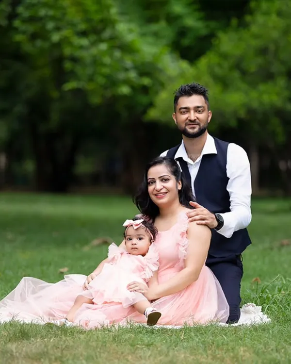 A classic family portrait taken in a lush green park. The family is dressed in coordinating pink and navy, sitting together for a beautiful outdoor photo.