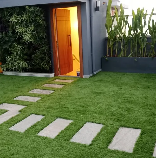 A complete terrace transformation featuring a lush artificial grass lawn with integrated stone pavers for a clean, modern pathway. This installation also includes a vertical garden accent wall by the entryway, creating a welcoming and vibrant outdoor living space that is entirely maintenance-free.