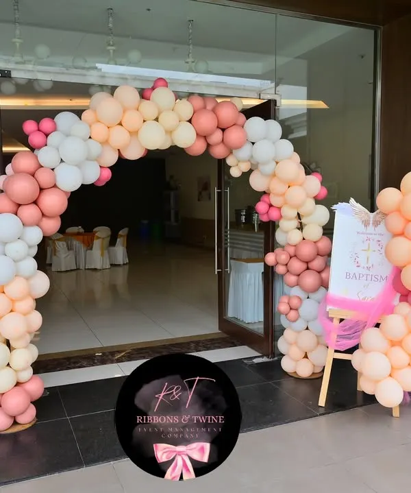 A beautiful balloon arch in shades of peach, pink, and white greets guests at the entrance for baby Sarah's baptism party.