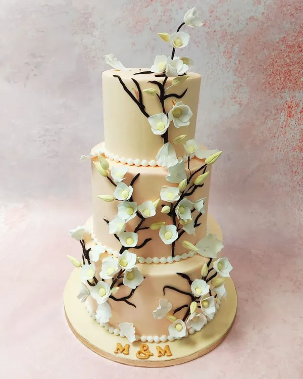 Our Three-Tier Cherry Blossom Wedding Cake is the epitome of elegance, with delicate, hand-crafted sugar blossoms cascading down the soft peach tiers.