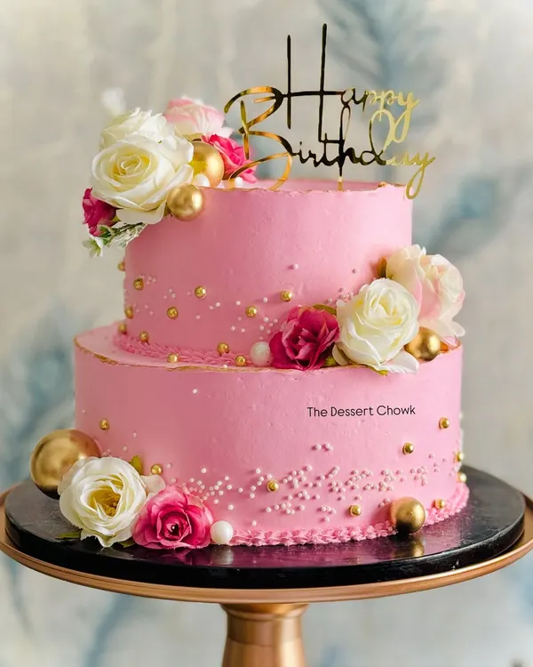 A beautiful two-tier custom birthday cake in a vibrant pink, decorated with white and pink roses and delicate gold pearls. This one was a pineapple flavor, perfect for a grand celebration.