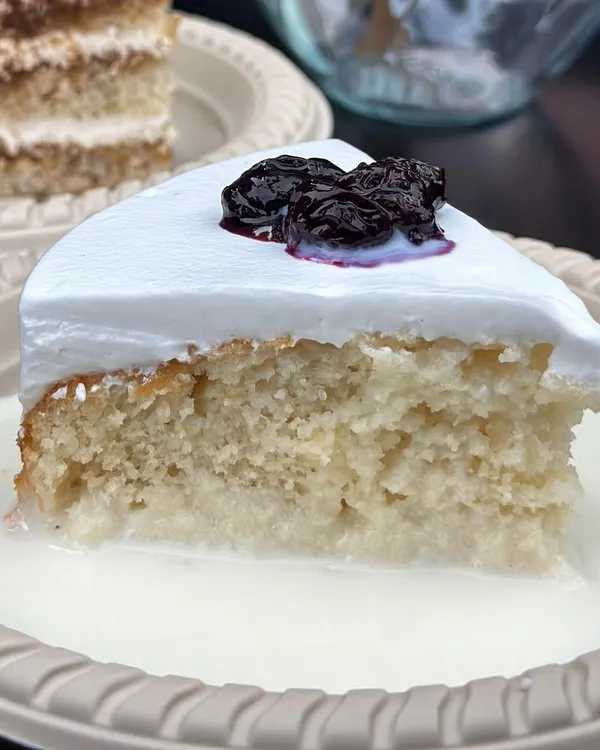A perfect slice of our eggless Milk Pastry. You can see the soft vanilla sponge soaking in the rich milk syrup, topped with whipped cream and our homemade berry compote.