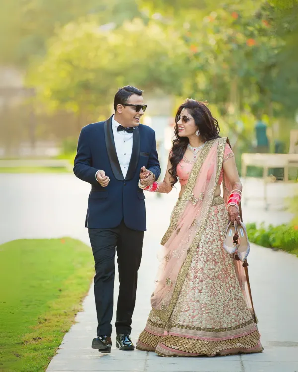 A fun, candid moment as the couple walks through a garden. The groom is dressed in a sharp tuxedo and the bride in a beautiful lehenga, showcasing a modern fusion look.