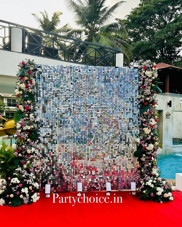 This shimmering silver sequin backdrop was created for a 75th birthday celebration. The wall is framed by columns of red and white flowers, creating a glamorous and celebratory photo spot by the pool.