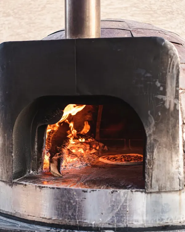 A glimpse inside our mobile wood-fired oven, where the magic happens. The intense heat creates that signature leopard-spotted char on the crust, cooking pizzas in just 90 seconds.