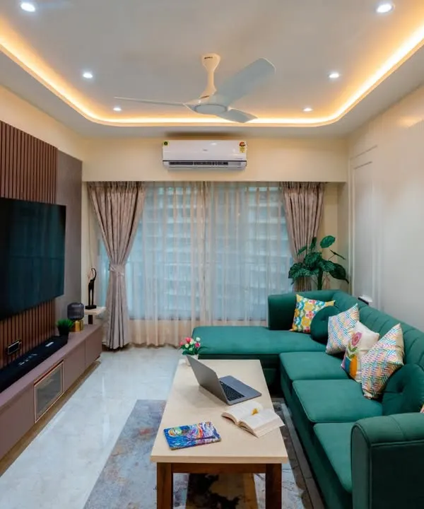 This modern living room features a striking emerald green L-shaped sofa. We balanced the bold color with a neutral palette, a fluted wooden panel for the TV unit, and warm cove lighting for a sophisticated feel.