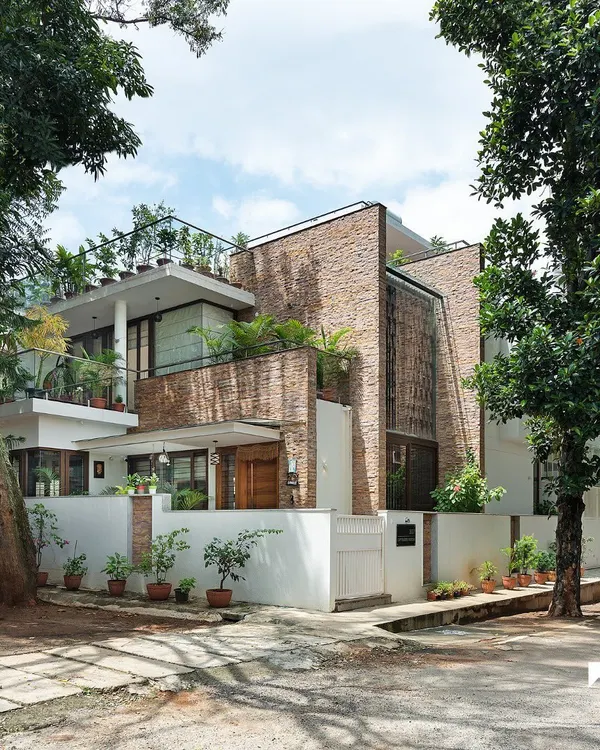 The exterior of the Twin Courtyard House, nestled among lush trees in Bangalore. The facade uses natural stone cladding and large openings to hint at the light-filled, nature-integrated spaces within.