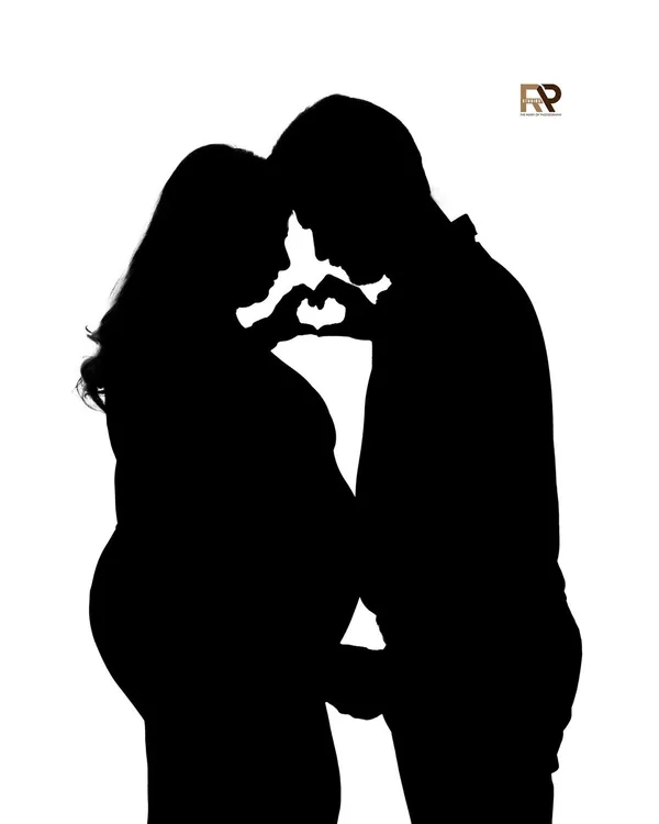 A beautiful silhouette of an expecting couple forming a heart with their hands over the baby bump. This artistic shot uses shadow and light to create a powerful symbol of love.