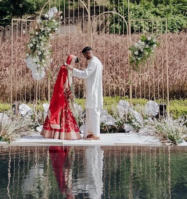 A breathtaking moment at a poolside wedding ceremony. The minimalist golden arch mandap, adorned with white florals, creates a stunning frame for the couple against the natural backdrop.