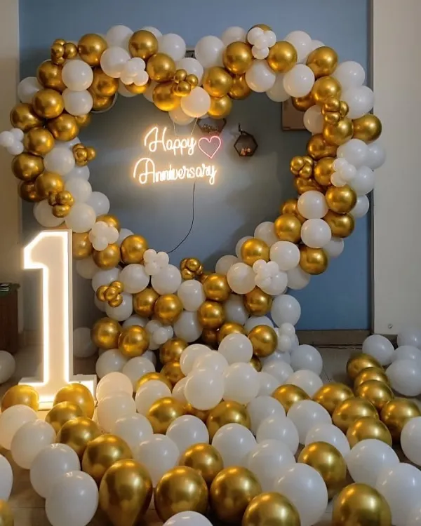 Celebrate your first anniversary with this stunning heart-shaped balloon arch in white and gold. The setup is completed with a "Happy Anniversary" neon sign and a large light-up number "1".