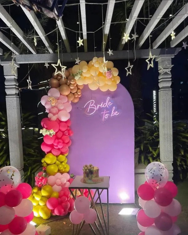 A lovely 'Bride to be' decoration on a terrace, featuring a purple backdrop, a colorful balloon garland, and hanging star lights.