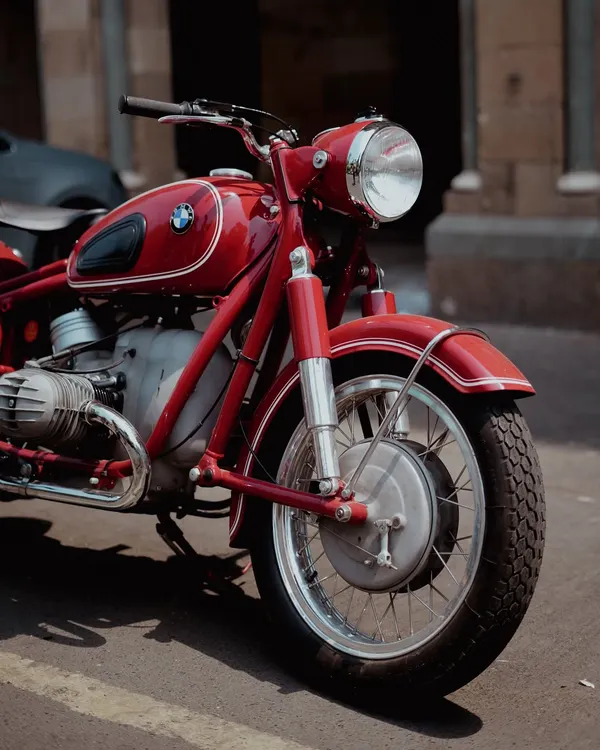 A detailed close-up of the front wheel and engine of a vintage red BMW motorcycle. This shot highlights the classic design and mechanical beauty of the bike, focusing on its historical craftsmanship.