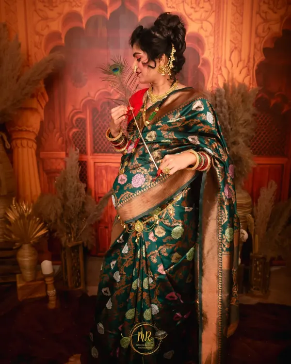 A stunning solo portrait of a mother-to-be in a traditional green and gold floral saree. The rich fabric and intricate details are highlighted against a warm, ornate backdrop.