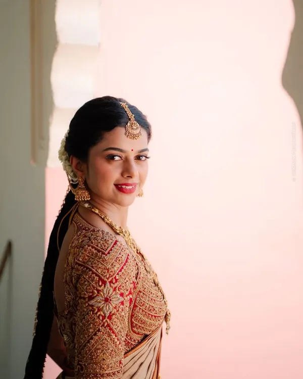 This red bridal blouse showcases heavy zardosi and sequin embroidery, crafted to perfectly match an off-white Kanchivaram saree. The detailed work on the sleeves makes it a standout piece for any muhurtham ceremony.