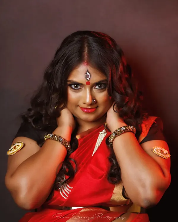 A powerful pose from our Devi-themed shoot. The makeup features intense, kohl-rimmed eyes, a bright red bindi with the third-eye detail, and a bold lip to create a look of divine strength and beauty.