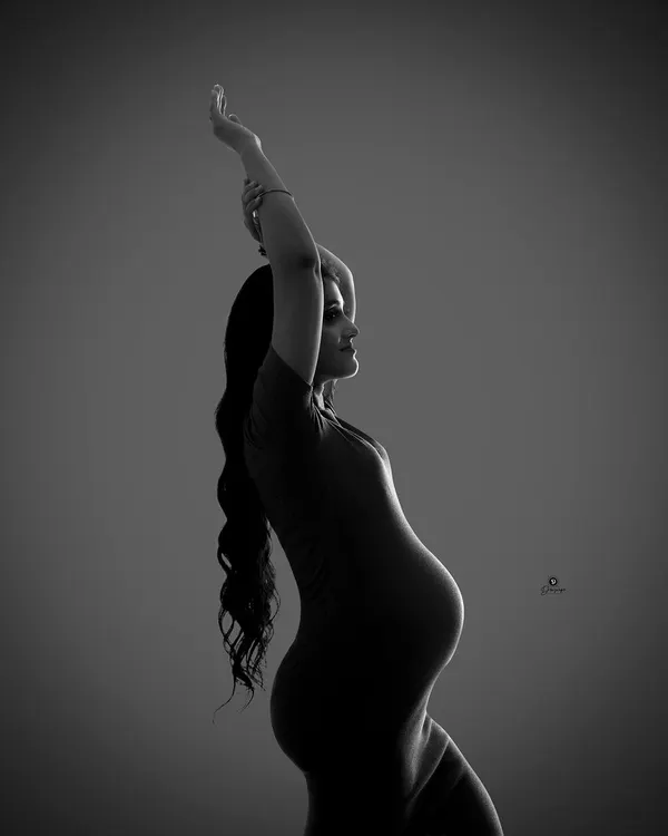 A graceful and artistic silhouette captured in black and white. The raised arm and elegant pose create a beautiful, dance-like shape, highlighting the contours of pregnancy in a unique way.