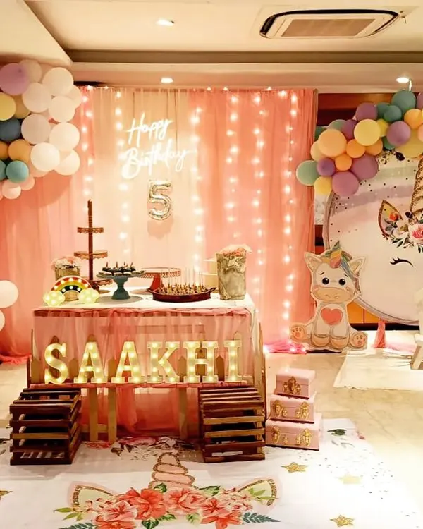 A full view of a unicorn-themed stage I designed, featuring a pastel rainbow balloon arch and custom unicorn cutouts. The personalized light-up marquee letters and unicorn-themed floor mat tie the entire magical concept together for a picture-perfect celebration.