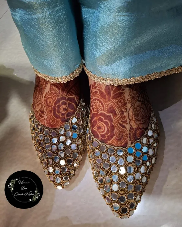 Your bridal look is complete with beautifully adorned feet. This design peeks out elegantly from a pair of traditional mirror-work juttis.