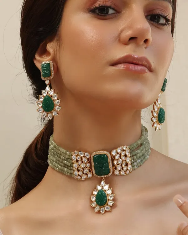 Welcome to Emrosia. This stunning set features a carved emerald choker with floral polki motifs and matching drop earrings, embodying the soul of the collection.