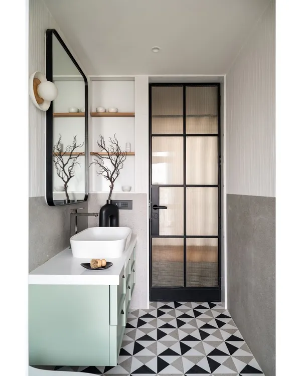 This master bath features a subtle interplay of nexion stone tiles and white fluted accents. The design is complemented by a mint green vanity with a pristine white marble countertop and a sleek black metal-framed mirror.