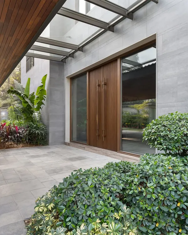 The main entrance of the K Residence, featuring large teak doors by Artius Glulam set within a stone-clad facade. The design of the entrance porch creates a welcoming transition from the lush landscaping to the home's interior.
