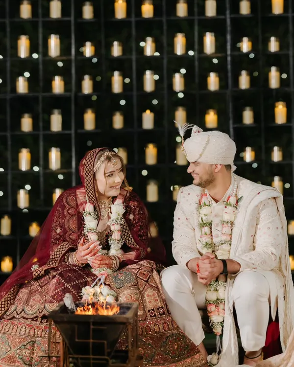 By the sacred fire, against a wall of candles, the couple shares a quiet moment during their pheras. This is where promises are made and forever begins.