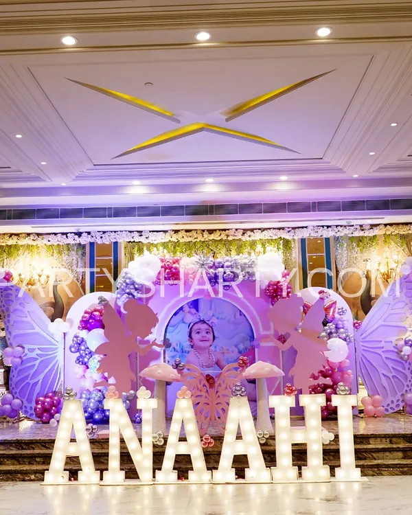A full stage view of a fairy and butterfly-themed birthday, featuring large, illuminated marquee letters spelling the child's name, whimsical fairy wing backdrops, and pastel balloon arrangements.