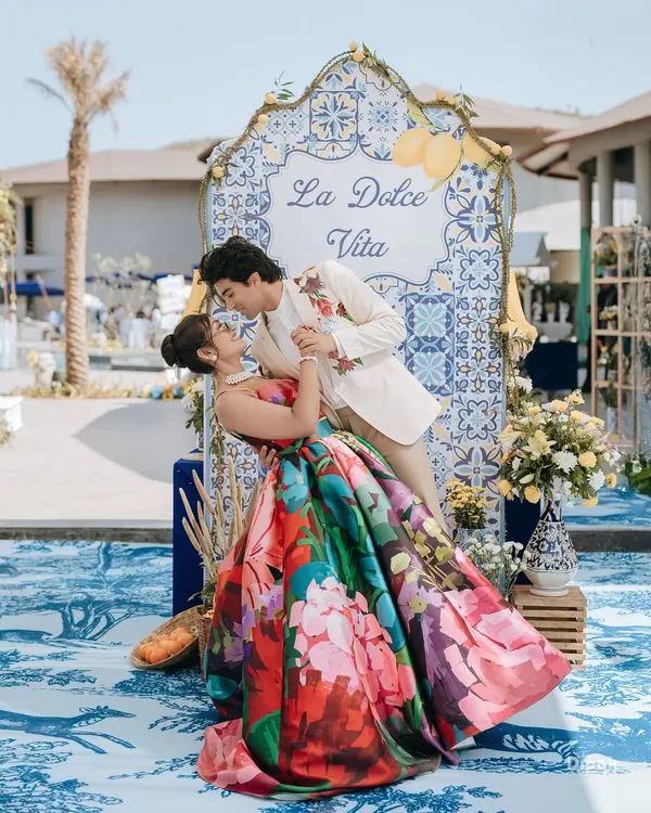 A vibrant and romantic shot from a "La Dolce Vita" themed carnival event. The couple's colorful outfits and the beautiful decor showcase a fun and stylish pre-wedding celebration.