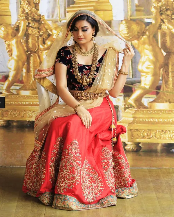 A truly royal bridal look, this ensemble pairs a deep navy velvet blouse with a vibrant red lehenga. The look is completed with a classic gold kamarbandh and dupatta, making it perfect for a traditional wedding ceremony.