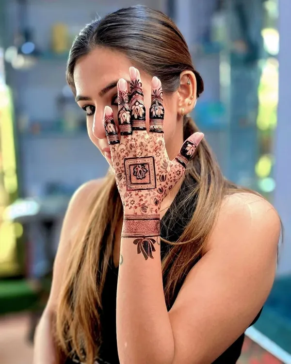 A happy client showing her modern, elegant mehandi. The design features a central square motif with delicate patterns and beautiful lotus designs on the fingers and wrist.