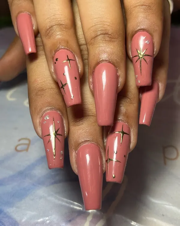 A classy and elegant set of long, coffin-shaped nails in a dusty rose color, adorned with delicate, hand-painted gold stars.