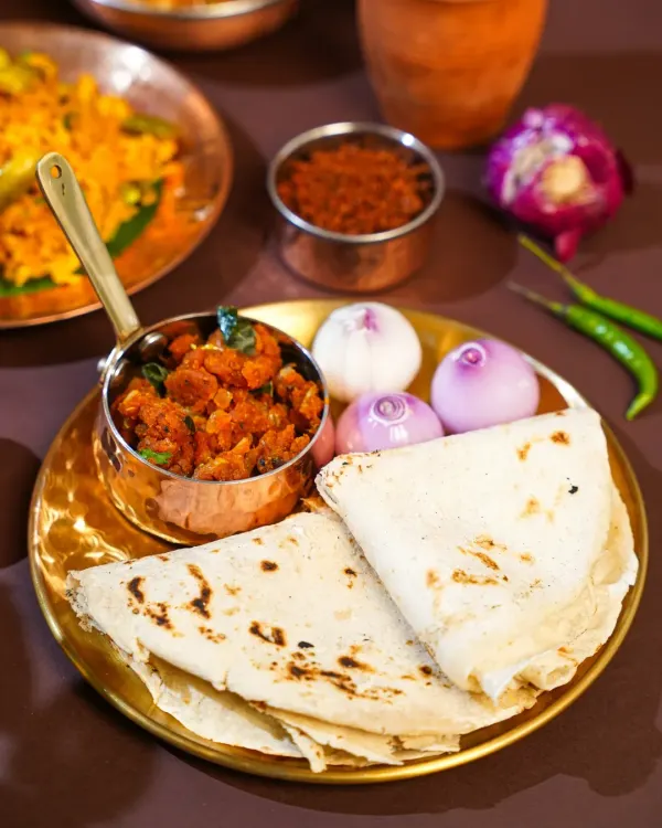 A rustic plate of authentic Maharashtrian Zunka Bhakar, served with raw onions and chili. The simple, earthy styling on a brass plate evokes the feeling of a traditional village meal.