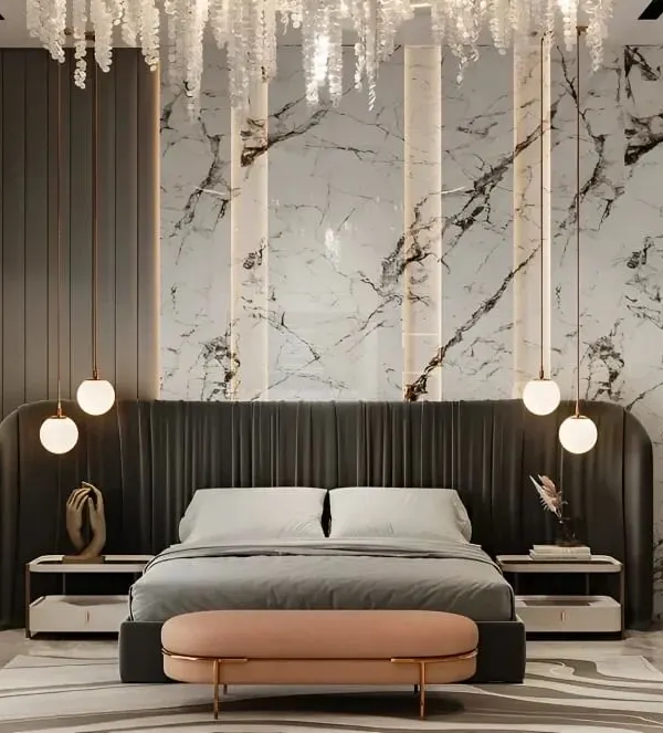 A luxurious master bedroom featuring a floor-to-ceiling upholstered headboard set against a dramatic marble accent wall. Integrated vertical lighting and hanging pendant lights create a sophisticated ambiance, highlighting our expertise in creating bespoke bedroom furniture and lighting schemes.