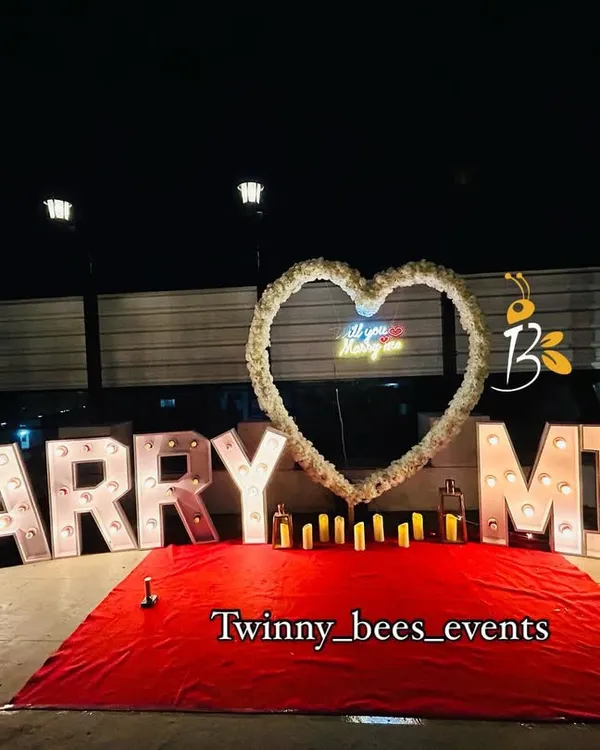 A classic and bold proposal setup. We use large, bright marquee letters that spell out "MARRY ME" with a beautiful floral heart and candles to create a grand romantic gesture.