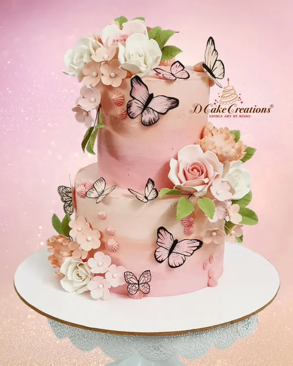 A beautiful two-tier cake in shades of pink, adorned with delicate sugar flowers and wafer paper butterflies. This design is perfect for birthdays, bridal showers, or any elegant celebration.