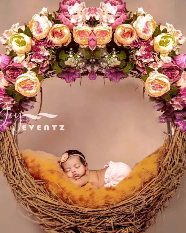 A newborn baby girl sleeps peacefully in a beautiful floral nest prop. This setup uses a rustic twig nest adorned with a halo of pink and cream peonies, creating a delicate and artistic portrait.