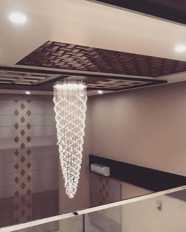 A stunning, multi-tiered crystal chandelier hangs in a double-height space, drawing the eye upward. The ceiling above features a 3D wooden pattern, adding another layer of texture and luxury.